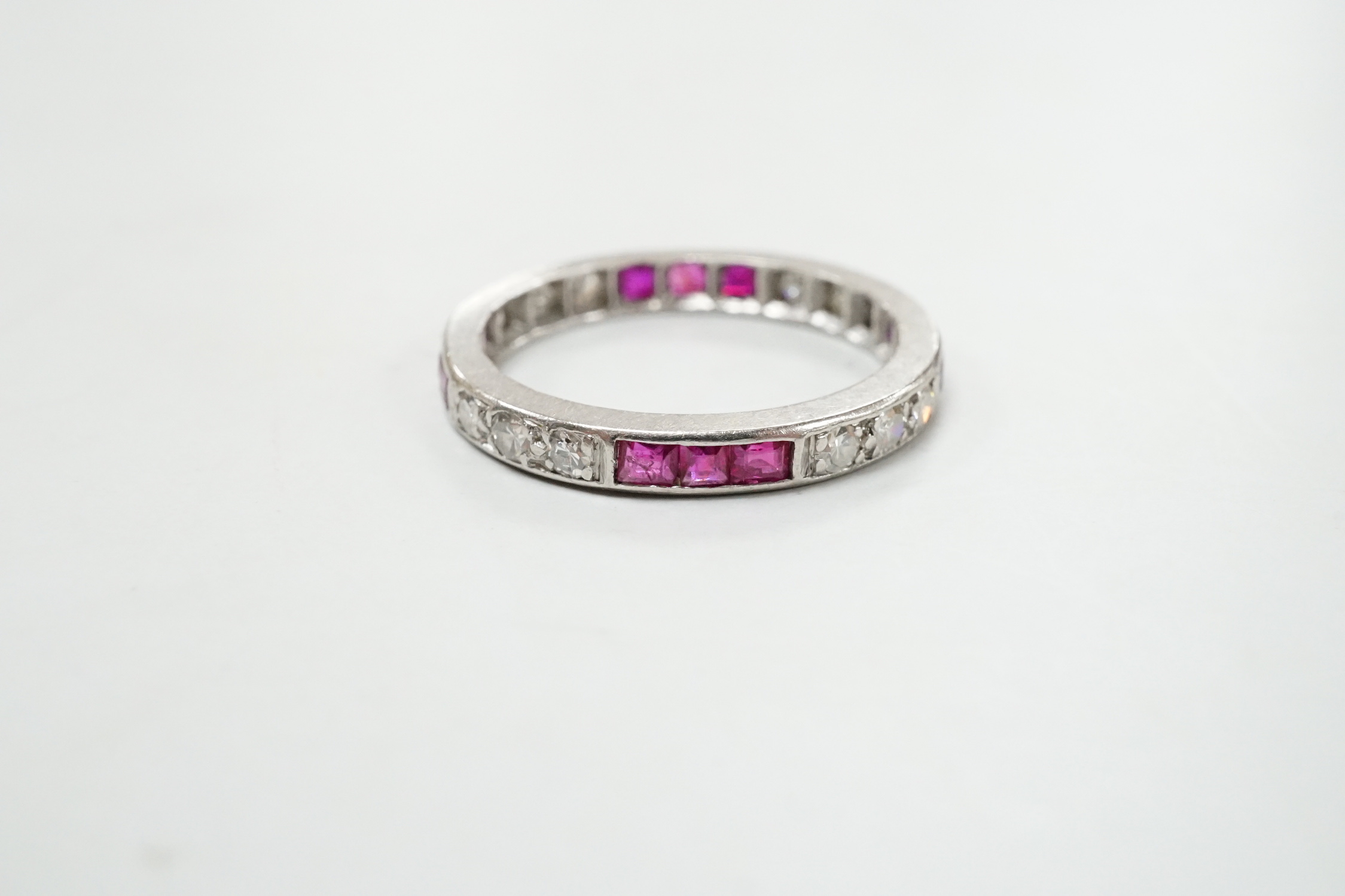 A white metal, ruby and diamond set full eternity ring, size L/M, gross weight 3.1 grams.